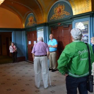 A tour group in the Historic Lobby of the Colonial Theatre stand under the golden ceiling and listen to Bill Munn conduct a tour.