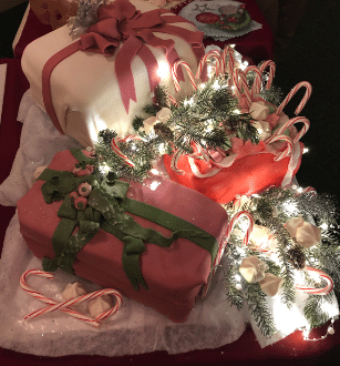 Three cakes in the shape of presents are displayed surrounded by lights and candy canes.