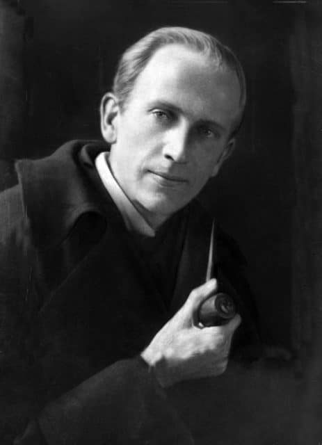 Picture of A. A. Milne partially turned to the camera holding a pipe with a wry smirk. 