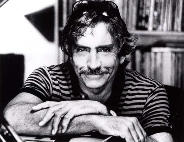 A young Edward Albee smiling with his arms crossed on a desk.